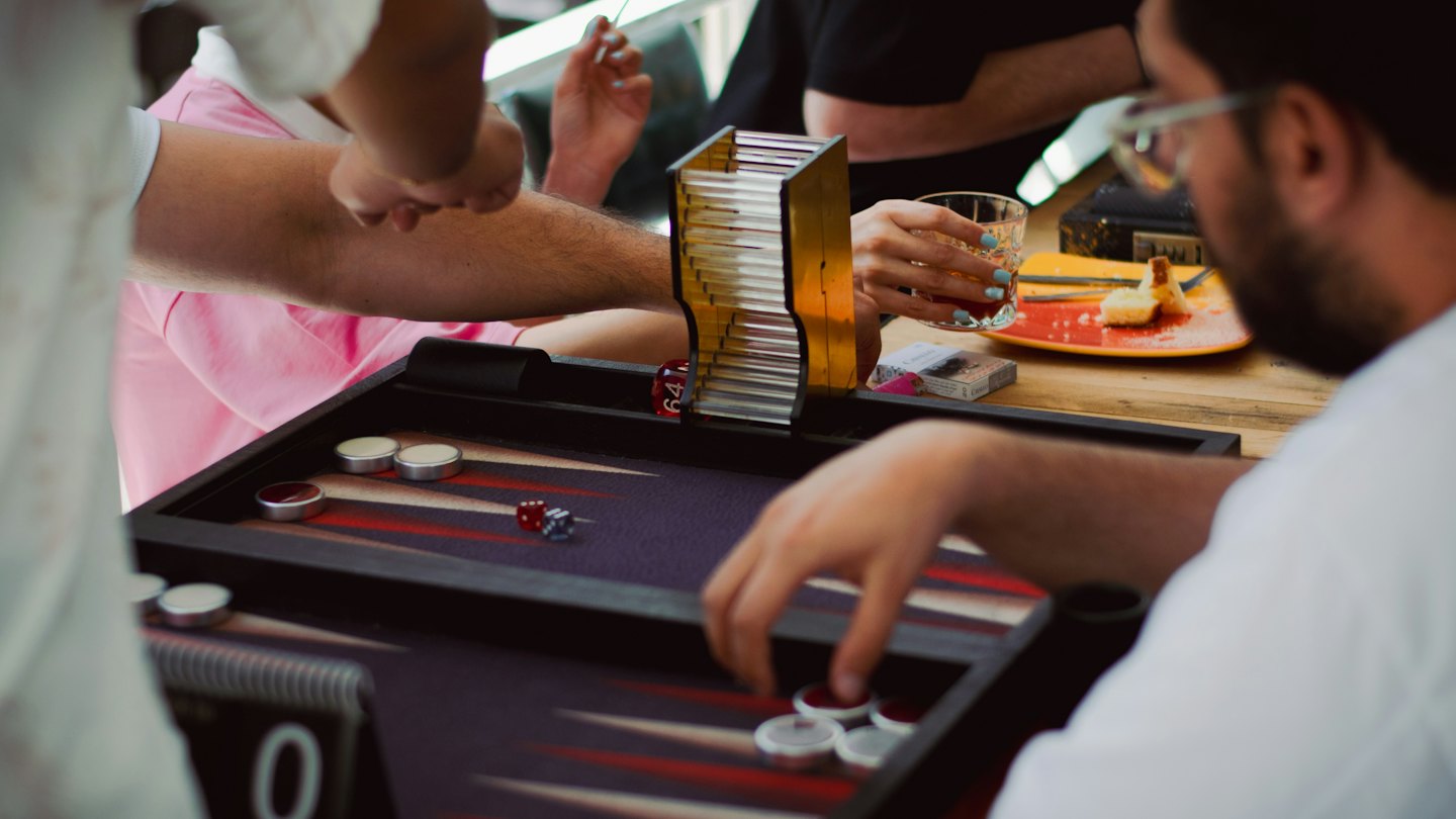 Friends playing a game of backgammon on a wooden table.