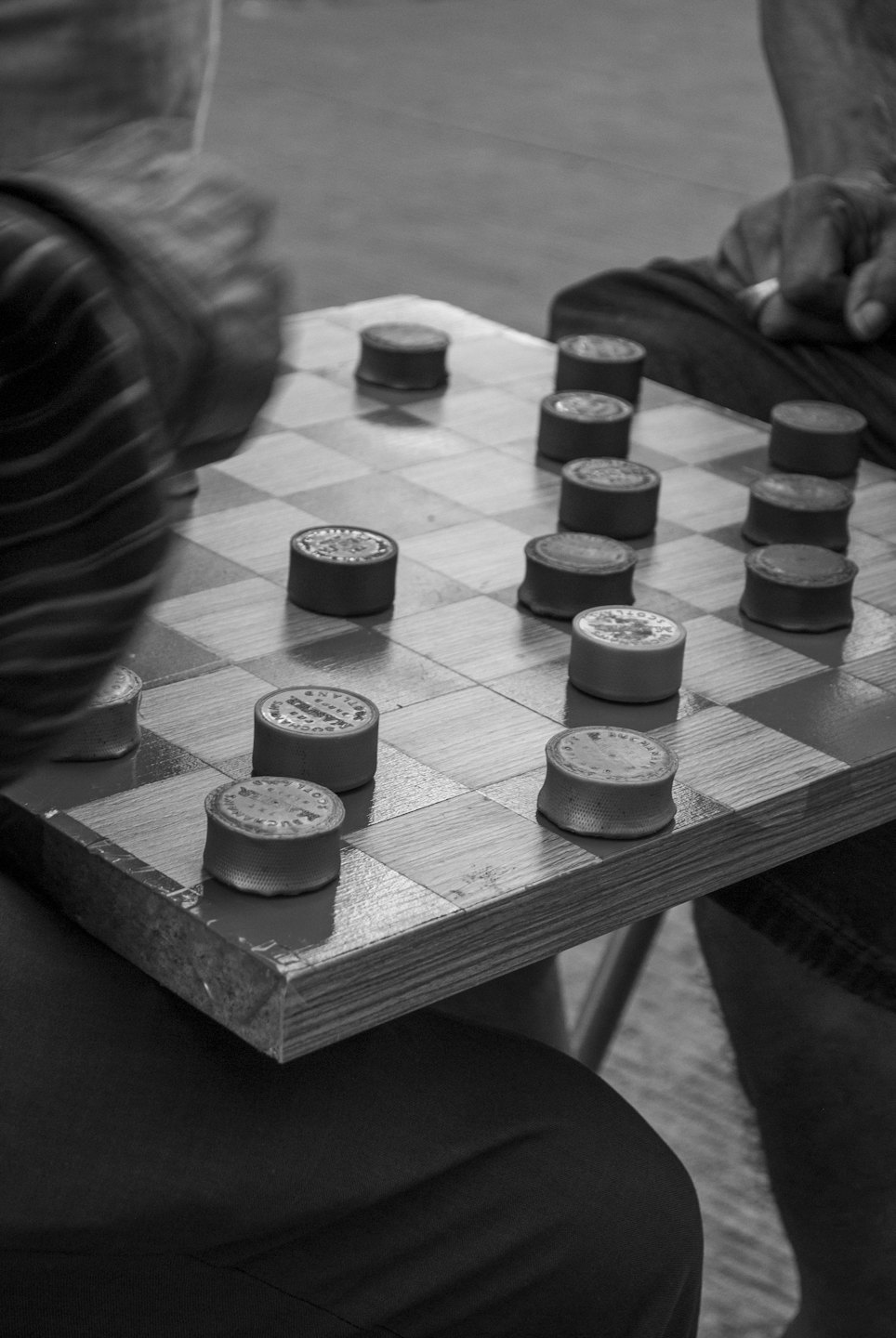 Two people playing a game of checkers on a wooden board.