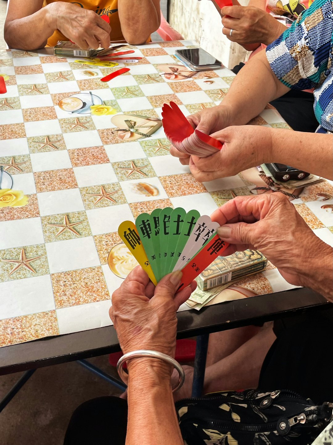 People playing a board game with numbered tiles at an outdoor table.